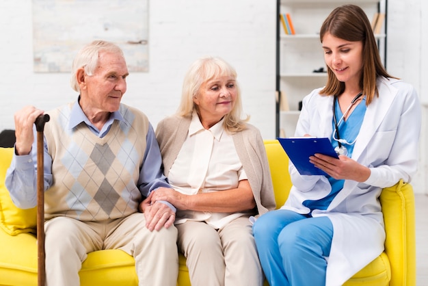 Nurse sitting with old man and woman on sofa