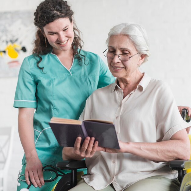 nurse standing behind the disabled senior woman reading book