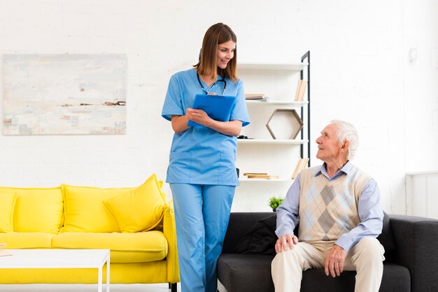 Free photo nurse talking to old man sitting on black sofa