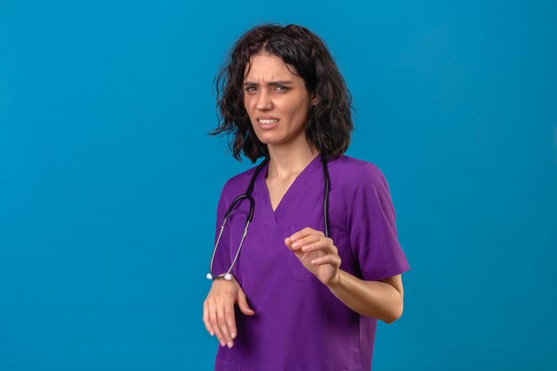 nurse wearing uniform and stethoscope raising palms in stop and rejection gesture disgusted expression on isolated blue