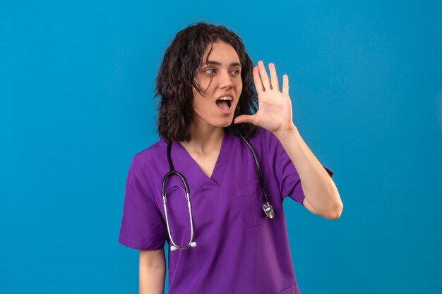 격리 된 파란색에 입 근처 손으로 누군가를 호출 유니폼과 청진기를 입고 간호사