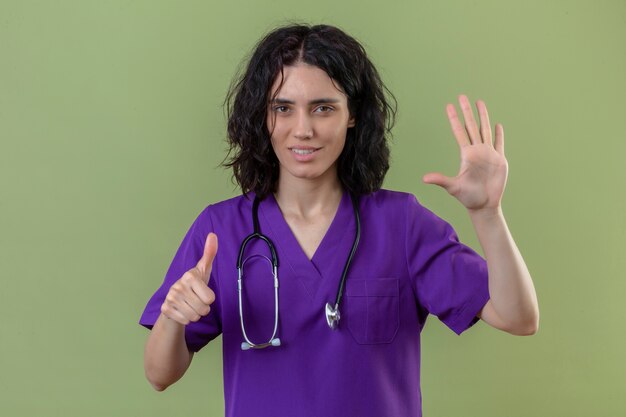 간호사 유니폼과 청진기를 입고 격리 된 녹색에 5 번과 엄지 손가락을 보여주는 미소