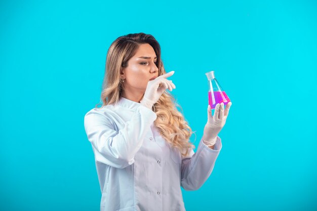 Nurse in white uniform holding a chemical flask with pink liquid and feels confused.