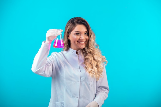 Nurse in white uniform holding a chemical flask with pink liquid and feels positive.