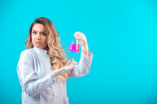 Nurse in white uniform holding a chemical flask with pink liquid and looks doubtful.