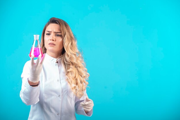 Nurse in white uniform holding a chemical flask with pink liquid and thinking. 