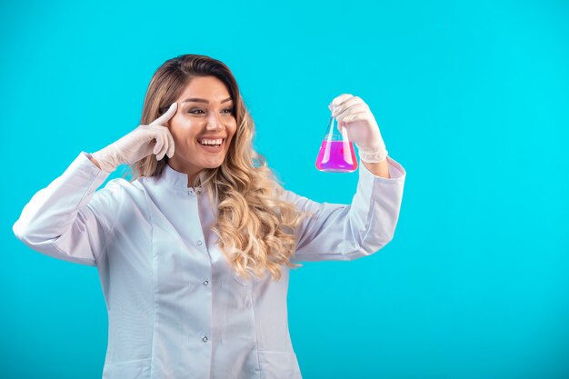 ピンクの液体で化学フラスコを保持している白い制服を着た看護師。