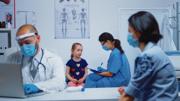 Nurse with protection mask writing child data on clipboard during covid-19. Physician specialist in medicine providing health care services consultation, treatment, examination in hospital cabinet