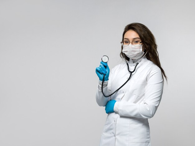 Nurse with stethoscope in her hand in white medical uniform and blue gloves