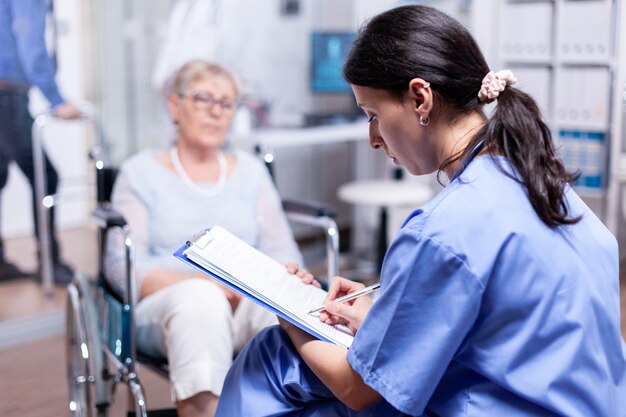 건강 진단 후 휠체어에 장애인 노인 여성을 위한 처방전을 작성 하는 간호사