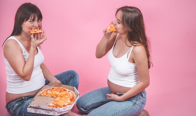 nutrition concept, pregnant women eating pizza on a pink wall