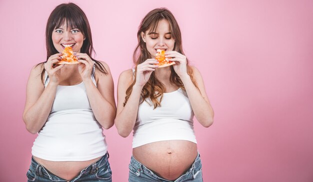 nutrition concept, pregnant women eating pizza on a pink wall
