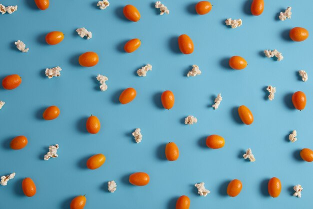 Nutritional orange unpeeled cumquat fruit containing vitamins and popcorn isolated over blue background. Ripe healthy fruit for your nutrition. Raw diet concept. Selective focus. Nagami variety