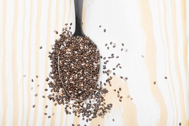 Nutritious chia seeds on a spoon, wooden background.