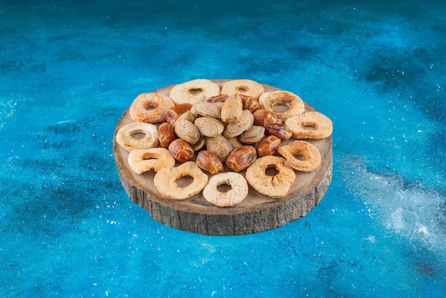 Nuts and dried fruits on a board on the blue surface