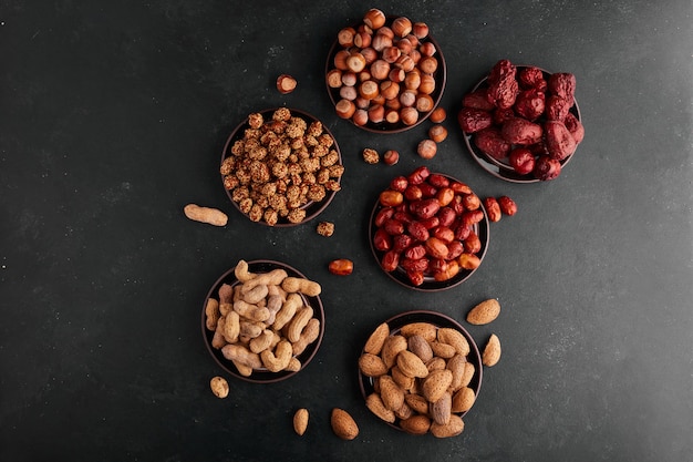 Nuts and snacks in black saucers, top view. 