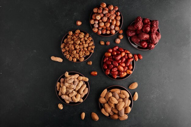 Nuts and snacks in black saucers, top view. 