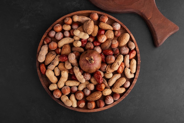 Орехи в деревянном блюде в центре на черной поверхности.