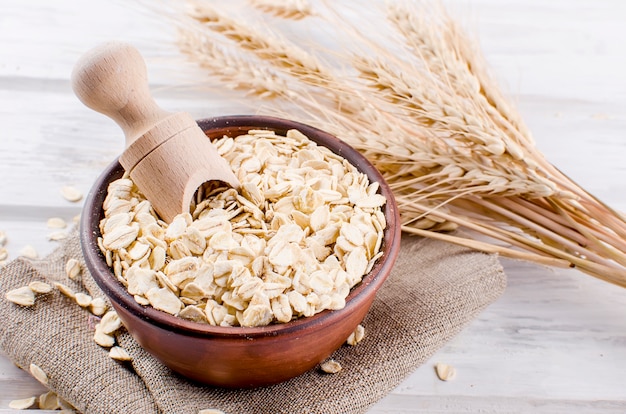 Oat flakes  in ceramic bowl and wooden spoon and spikelets Premium Photo