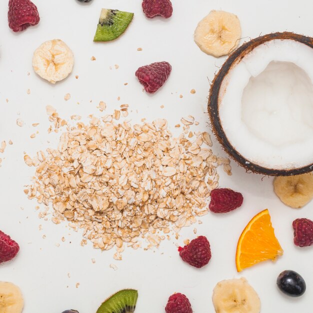 Oat flakes; raspberry; grapes; slice of lemon and banana and halved coconut on white background