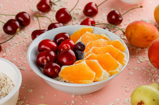 Oat flakes with pear, apricot, orange, cherry, berries in bowl
