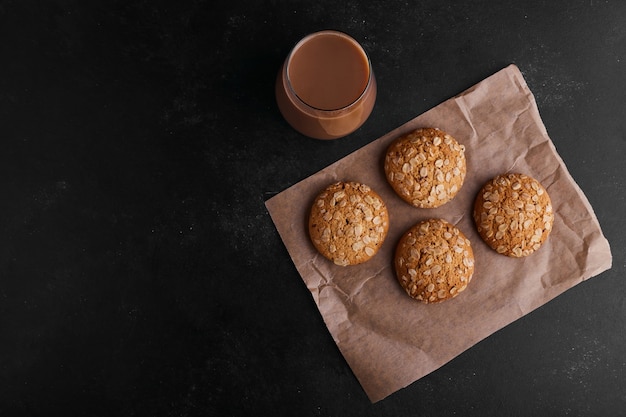 Oatmeal cookies on black background with a glass of hot chocolate, top view. 