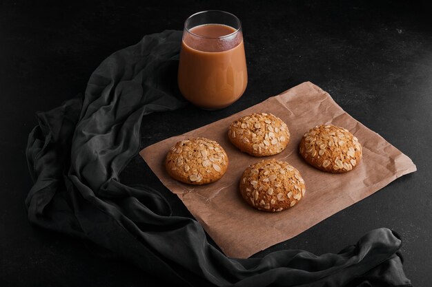 Oatmeal cookies on black surface with a glass of hot chocolate. 