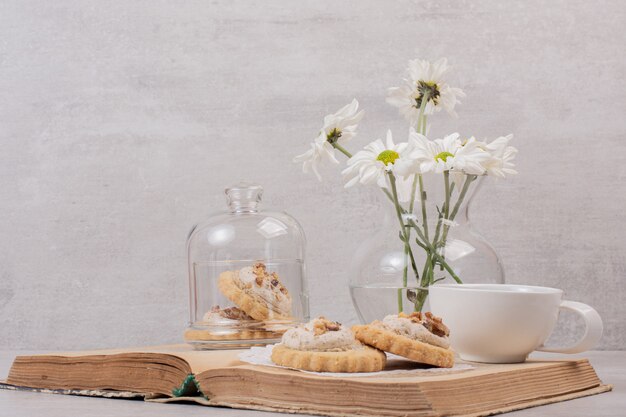 Oatmeal cookies, a cup and daisies on book.