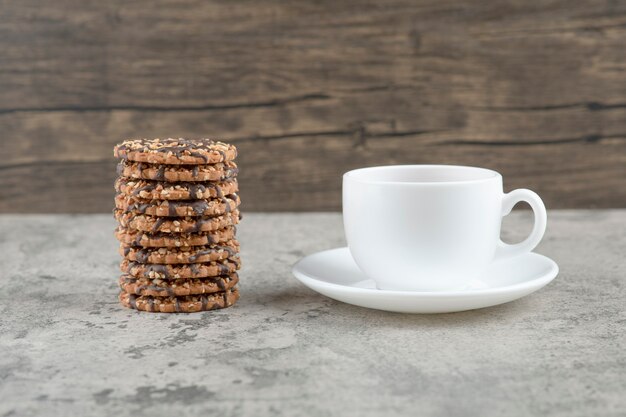 Oatmeal cookies with chocolate syrup with a cup of tea on a stone table .