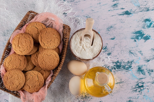 Oatmeal cookies in a wooden basket tray with ingredients around.