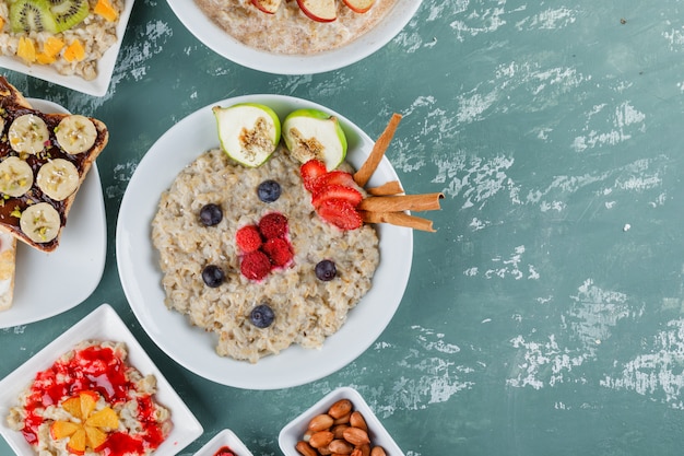 Oatmeal in plates with fruits, jam, sandwich, cinnamon, nuts