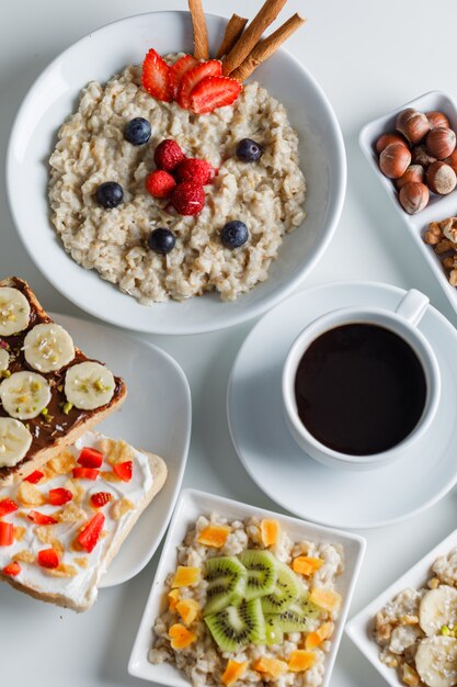 Oatmeal with berries, cinnamon, nuts, fruits, coffee, sandwich in plates