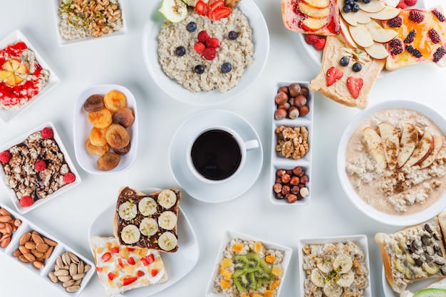 Oatmeal with fruits, nuts, jam, coffee, fruit sandwich, milk, cinnamon, dry apricots in plates