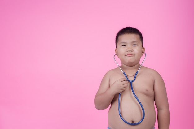 Тучный мальчик, который весит больше нормы на розовом фоне.