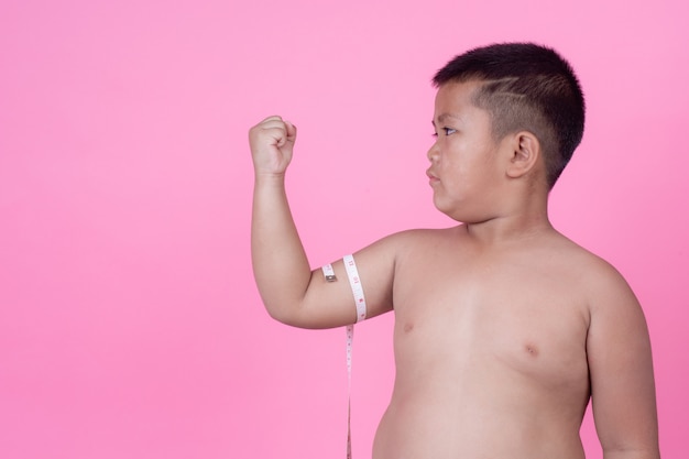 Тучный мальчик, который весит больше нормы на розовом фоне.