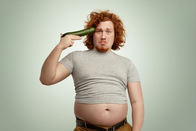 Obese overweight young redhead male ready to shoot himself out of improvised cucumber gun