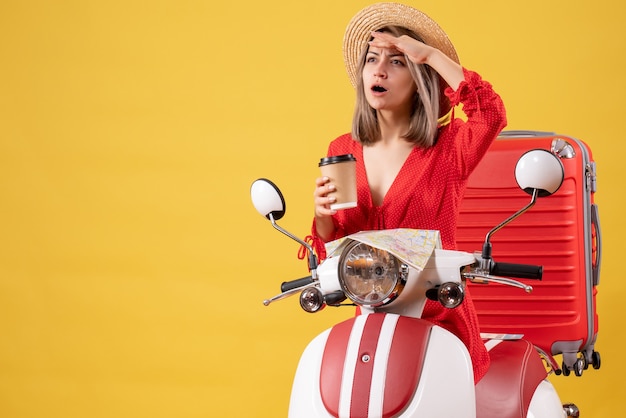 observing young lady in red dress holding coffee cup near moped