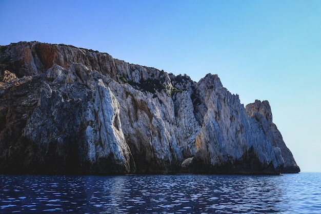 Ocean waves surrounded by the rocky cliffs gleaming under the blue sky