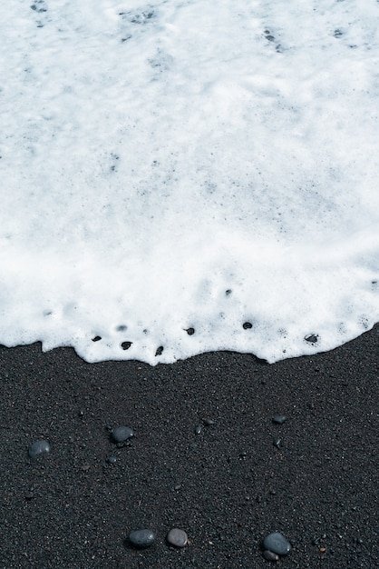 Foto gratuita onda oceanica con schiuma bianca rotola sulla spiaggia di sabbia nera con ghiaia. costa sabbiosa vulcanica di tenerife.