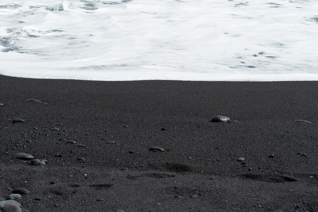Free photo oceanic wave with white foam rolls over black sand beach with pebble.tenerife voulcanic sandy shore.