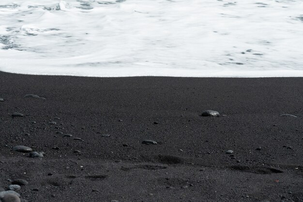 Oceanic wave with white foam rolls over black sand beach with pebble.Tenerife voulcanic sandy shore.
