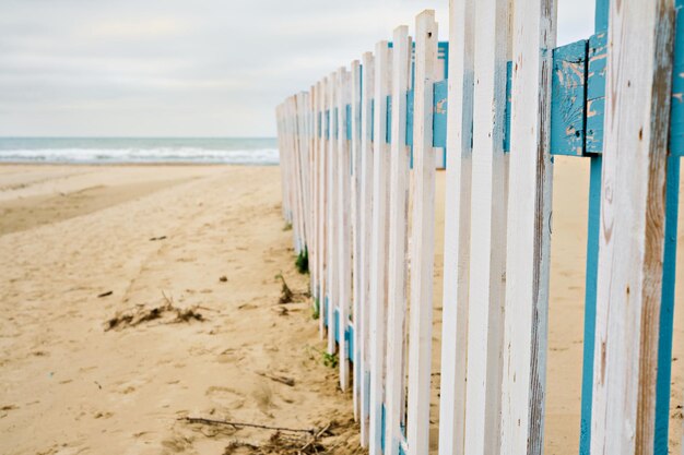 Отдых в межсезонье. Пустынный весенний пляж, забор перед общественным пляжем, облачное небо в ожидании дождя. Морской пляж в межсезонье, место для текста