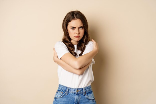 Offended angry woman cross hands on chest, frowning and sulking insulted, standing over beige background