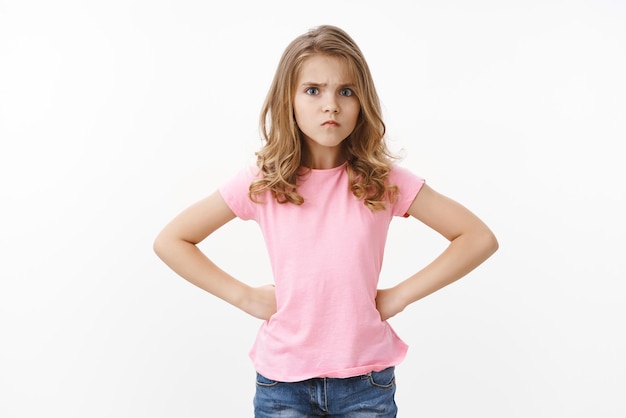 Offended cute sulking young blond little girl kid looking upset frowning hold hands hips insulted stare camera disappointed waiting apologies jealous brother ate her sweets white background