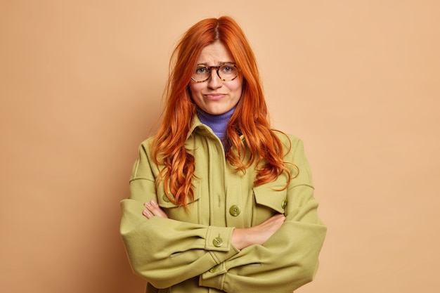 Free photo offended dissatisfied redhead young woman keeps arms folded waits for explanations from boyfriend has hurt feelings dressed in fashionable green jacket smirks face.