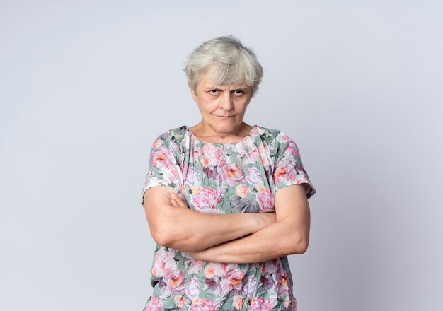 Offended elderly woman stands with crossed arms isolated on white wall