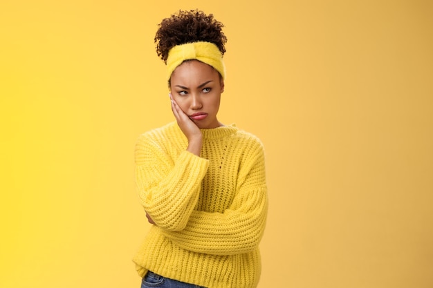 Offended gloomy grumpy pouting young african-american girlfriend feel irritated jealous frowning bothered sulking look away insulted unwilling talk somebody lean hand head standing yellow background.