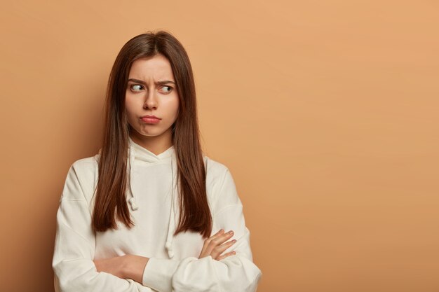 Offended insulted Caucasian woman looks angrily aside, keeps arms folded, frowns face and looks with dissatisfaction