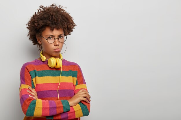 Offended upset curly woman with arms folded, gloomy face expression, stands sullen and disappointed