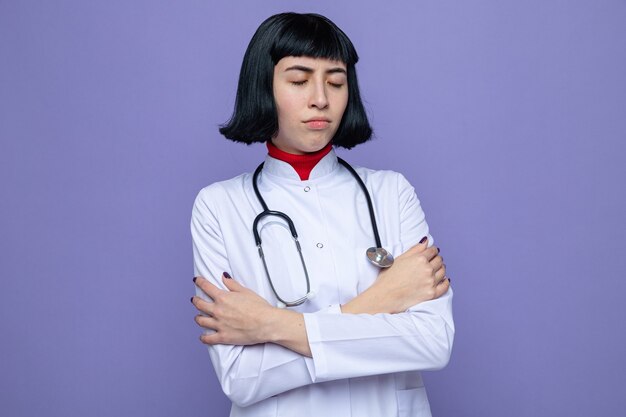 Offended young pretty caucasian girl in doctor uniform with stethoscope standing with crossed arms 